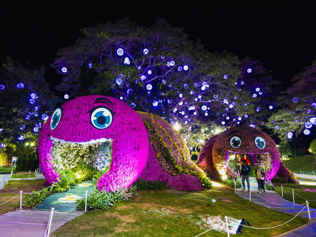 A large turtle-shaped structure made entirely of flowers serving as a walk-through tunnel for visitors.