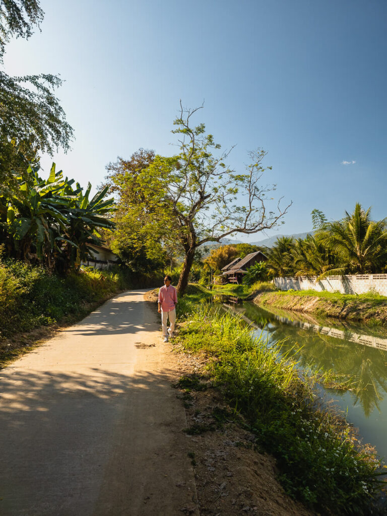 A traveler walking beside a peaceful river at a hidden cafe stop along the anti-clockwise Samoeng Loop route.