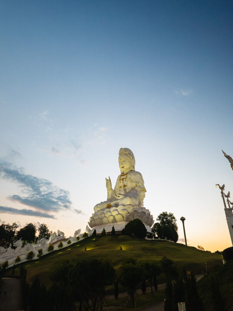 The massive white Guan Yin Buddha statue at Wat Huay Pla Klang illuminated by the golden sunset light.