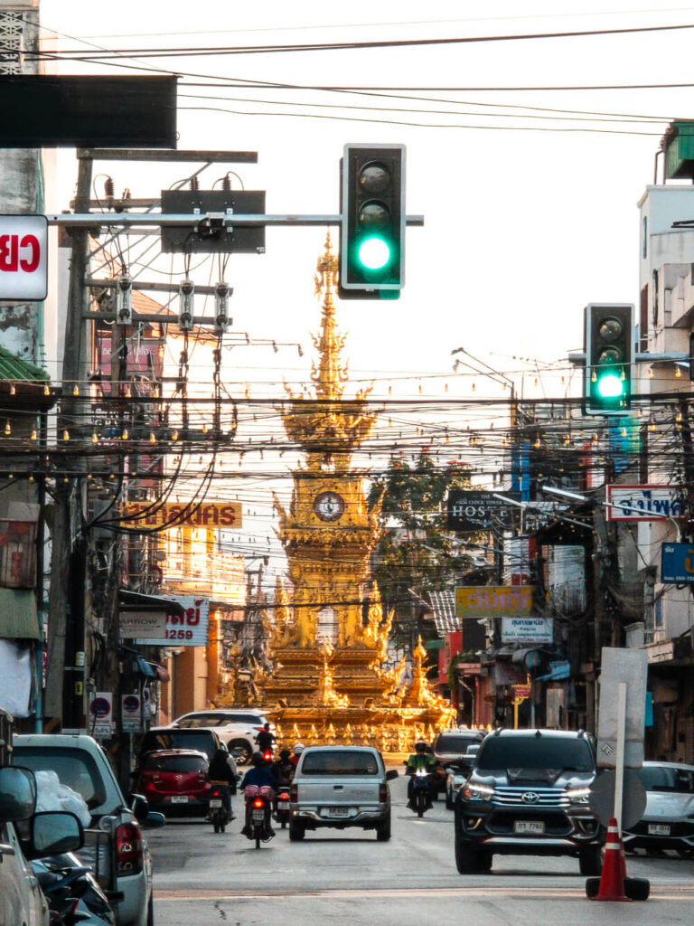 Busy city traffic and scooters riding near the famous gold Clock Tower in Chiang Rai.
