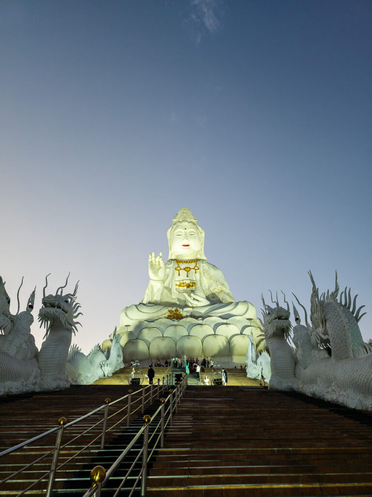 The massive 79-meter white Guan Yin Goddess of Mercy statue at Wat Huay Pla Kang standing tall just after a golden sunset in Chiang Rai.