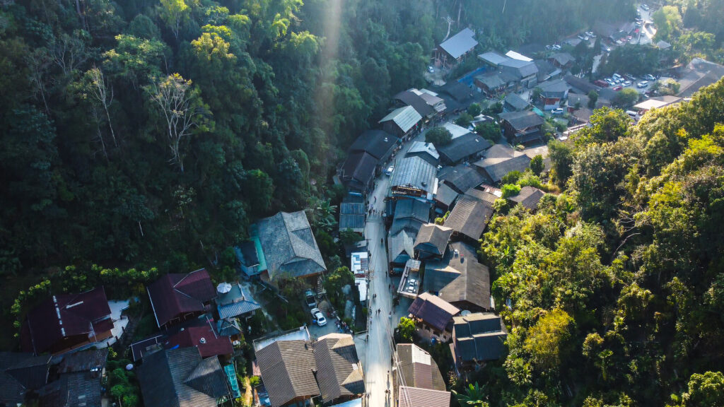A high angle drone shot showing the wooden houses of Mae Kampong Village nestled in the lush green mountains of Chiang Mai.