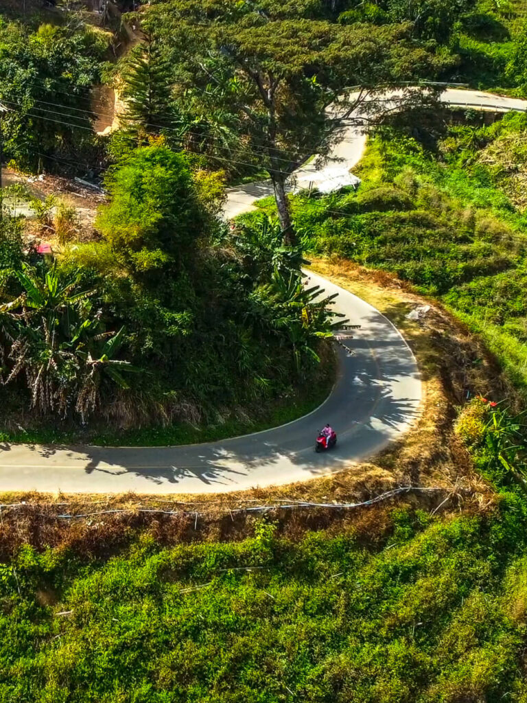 Drone aerial view of riding a rental scooter on the winding curves of the Samoeng Loop in Northern Thailand.