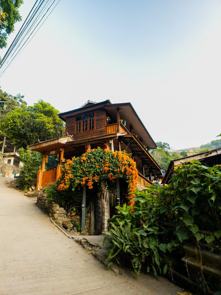 A charming traditional wooden house decorated with vibrant orange flowers near the village entrance.