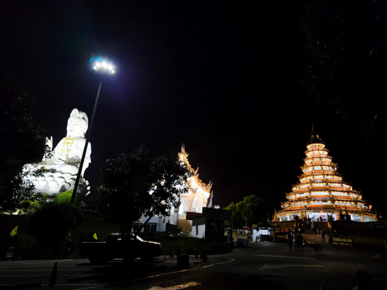Night panoramic view of the Wat Huay Pla Kang temple complex in Chiang Rai featuring the illuminated giant Guan Yin statue, the red nine-tier pagoda, and the main temple hall.