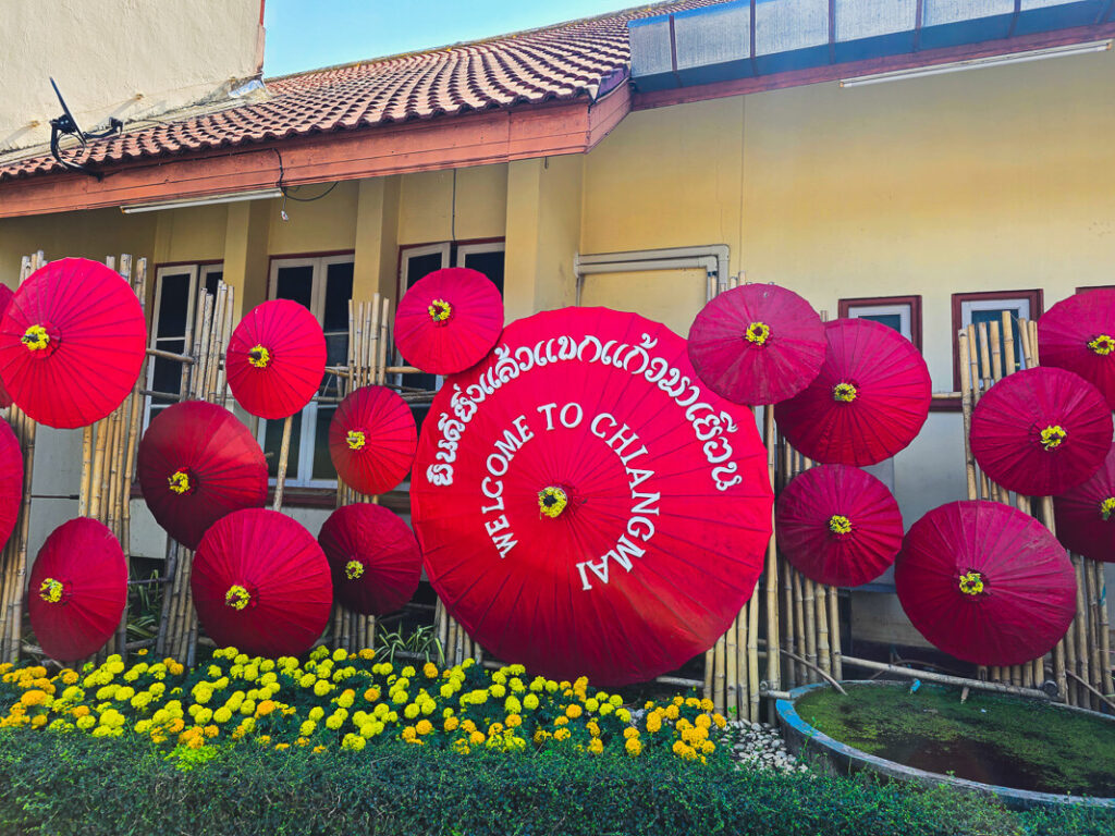 A colorful umbrella decoration with a Welcome to Chiang Mai sign for travelers riding a scooter in Northern Thailand.