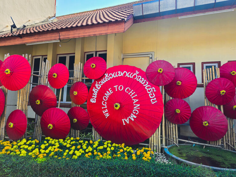 A colorful umbrella decoration with a Welcome to Chiang Mai sign for travelers riding a scooter in Northern Thailand.
