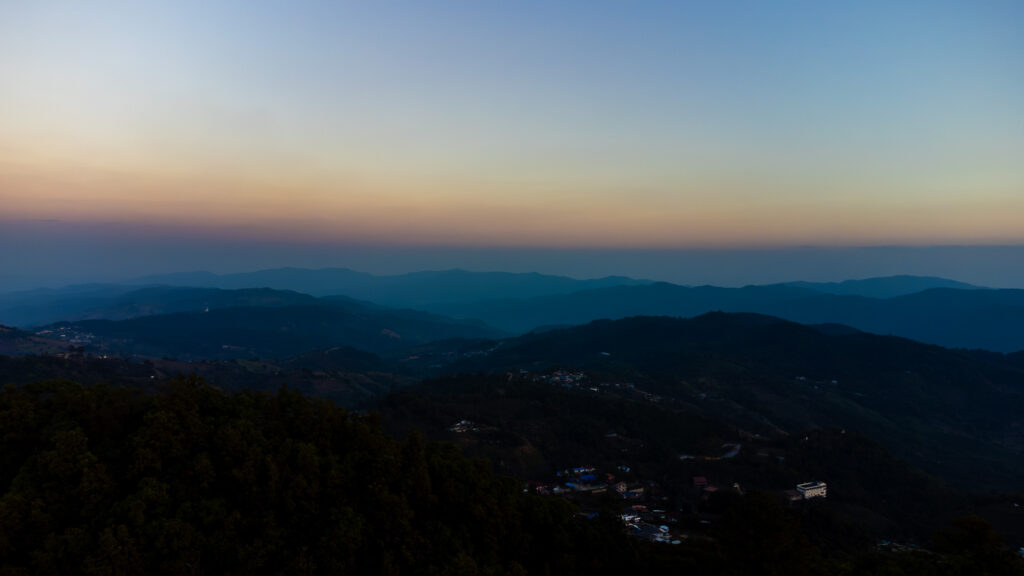 High-angle drone shot of the winding mountain roads and tea plantations in Mae Salong, highlighting the best time to visit Northern Thailand with clear blue skies.