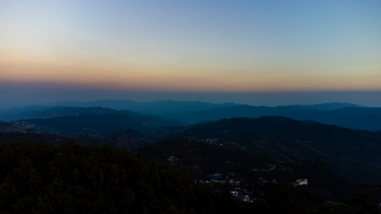 High-angle drone shot of the winding mountain roads and tea plantations in Mae Salong, highlighting the best time to visit Northern Thailand with clear blue skies.