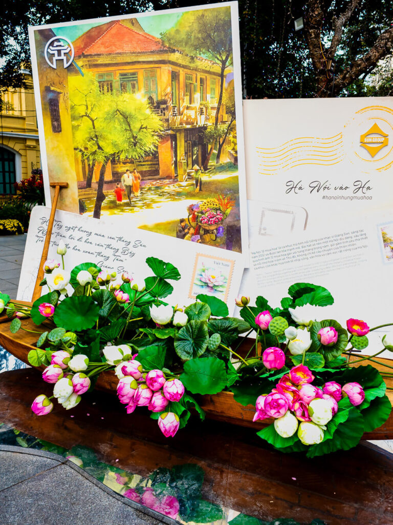 A festive street decoration near the Chieu Doi Do statue featuring a boat filled with bright flowers and oversized vintage postcards.