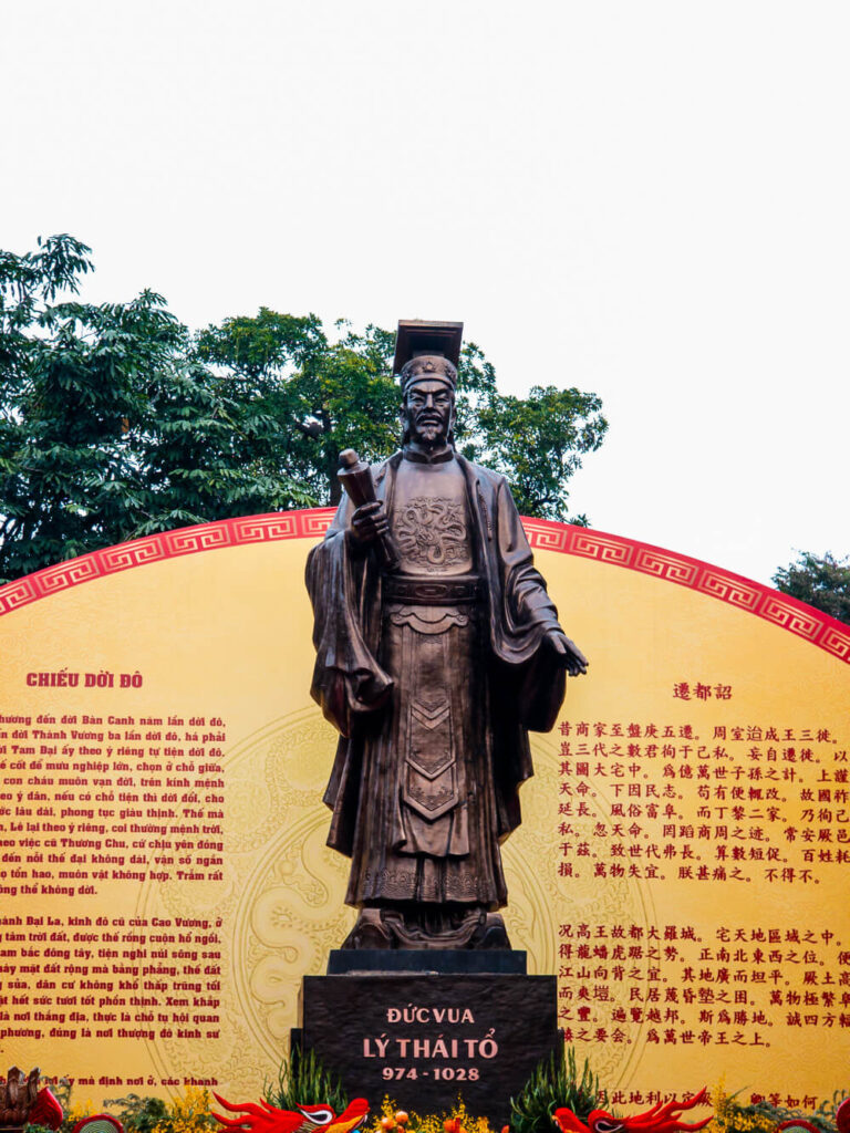 The Chiêu Dời Đỏ statue standing tall surrounded by a manicured garden near Hoàn Kiếm Lake.