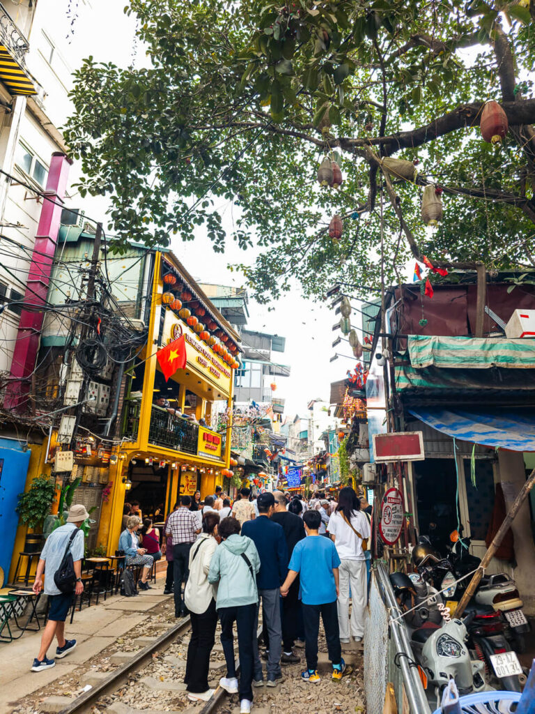 Tourists crowded tightly along the narrow tracks of Hanoi Train Street waiting for the train to pass by the local cafés.