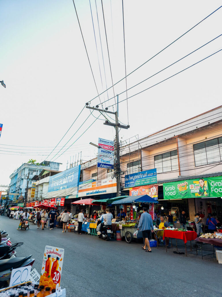 A vibrant scene inside a local Chiang Rai market showing vendors and locals interacting among stalls of fresh vegetables and local goods.
