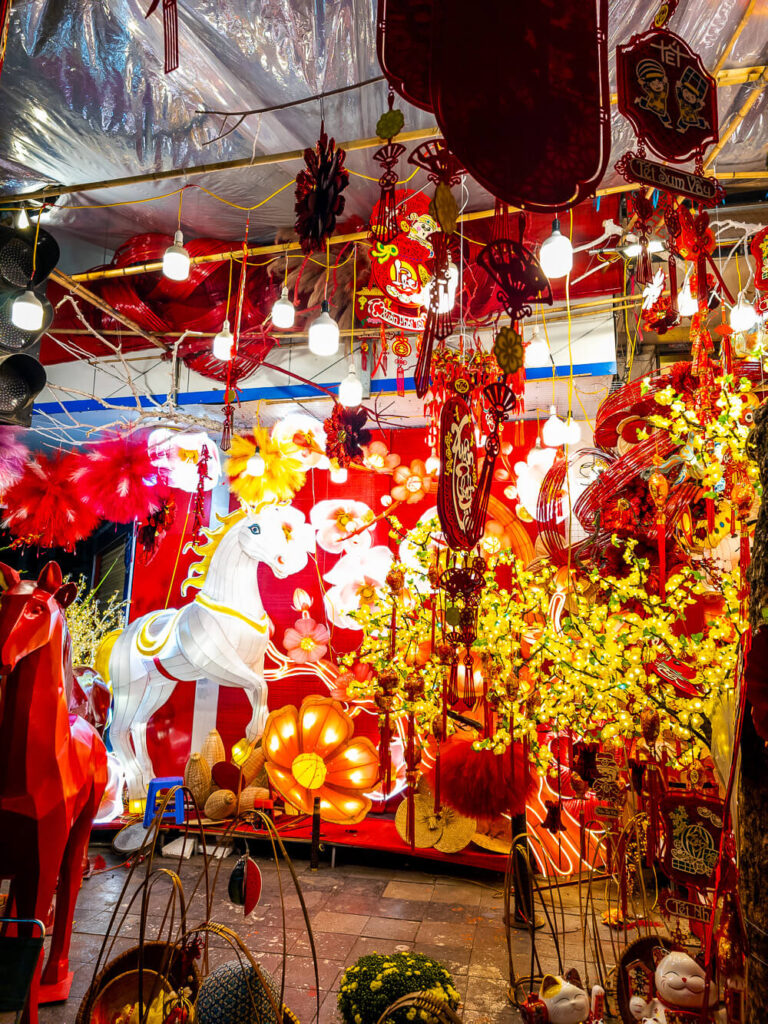 Bright neon lights and a horse light statue illuminating the crowded night market in the Hanoi Old Quarter.