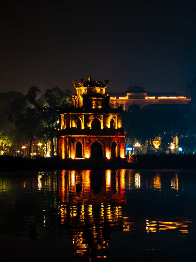 The vibrant and chaotic streets of Hanoi Old Quarter lit up at night with motorbikes and street food vendors.