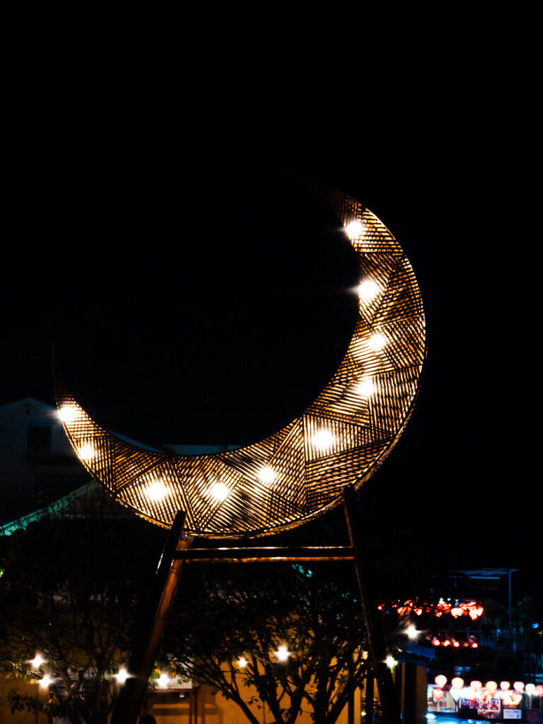 A glowing decorative moon structure illuminating the bustling night market streets in Hoi An Old Town.