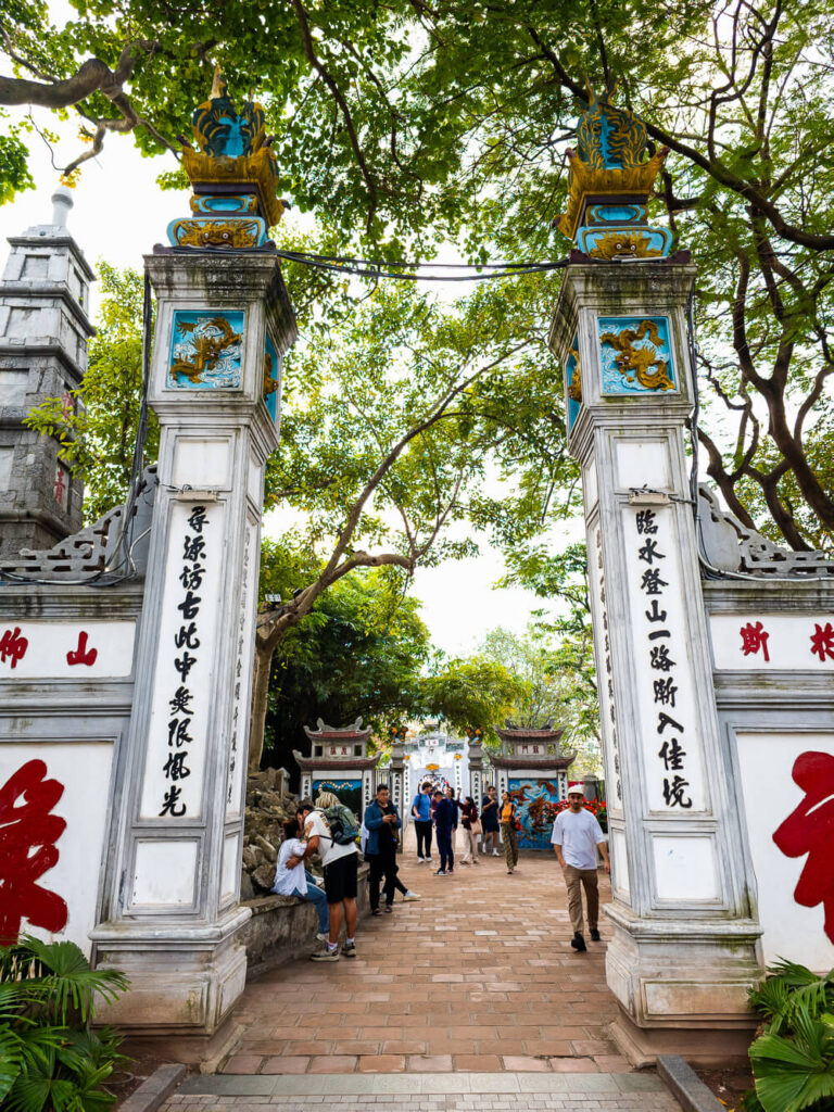 The traditional stone entry gate to Ngoc Son Temple surrounded by trees in central Hanoi.