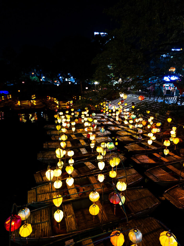 Traditional wooden rowboats docked at a calm lake in Ninh Binh under the dark night sky.
