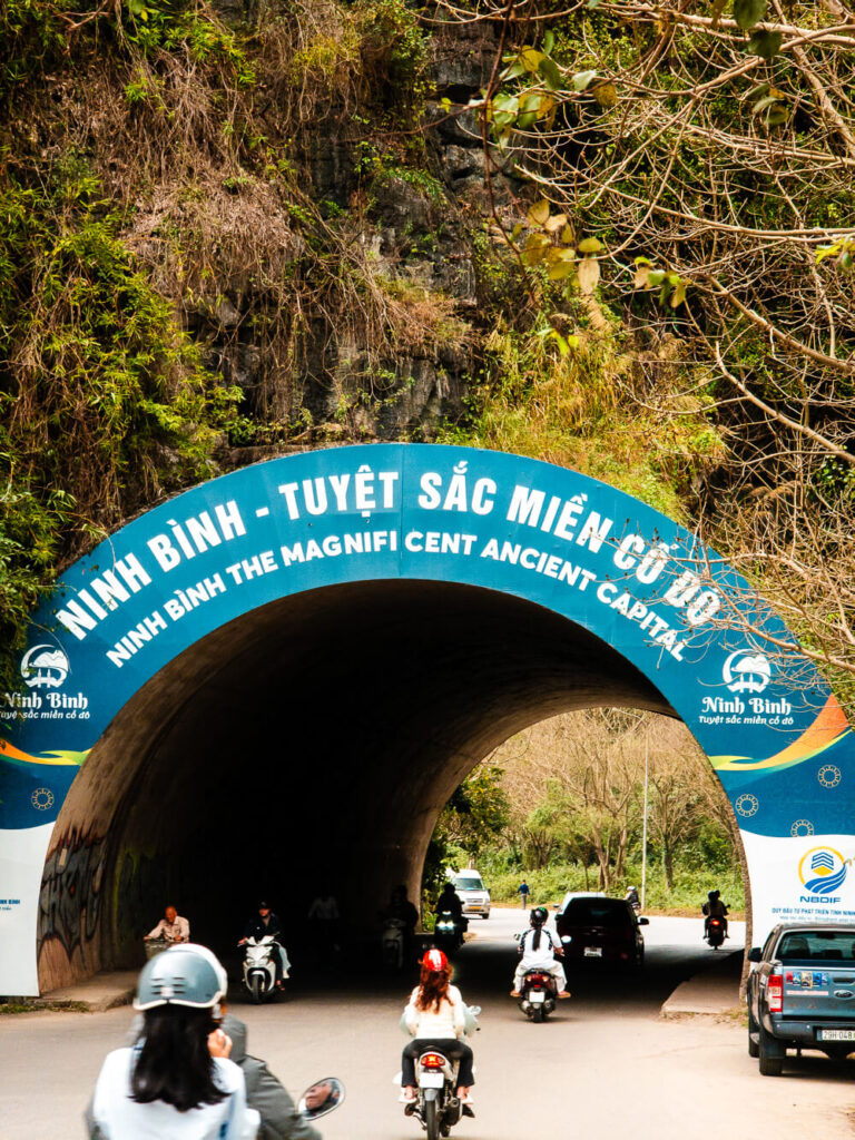 A dark stone entry tunnel leading into the dramatic limestone karst landscapes of Ninh Binh, Vietnam.