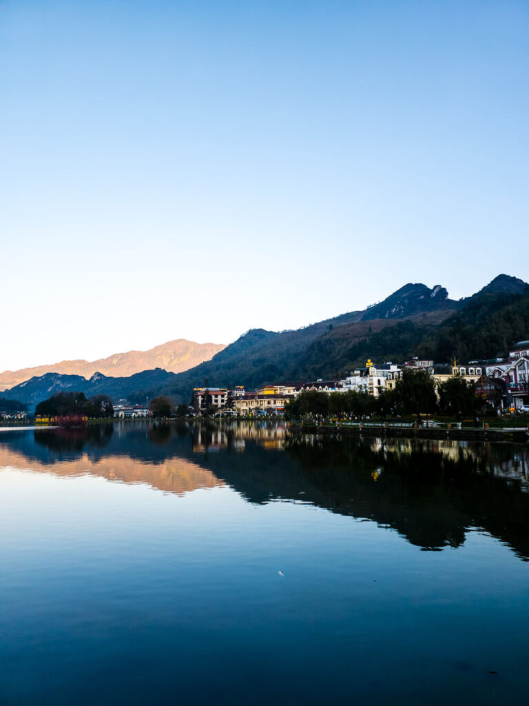 A view of the lake in the center of Sapa town with mountains and colorful buildings in the background.