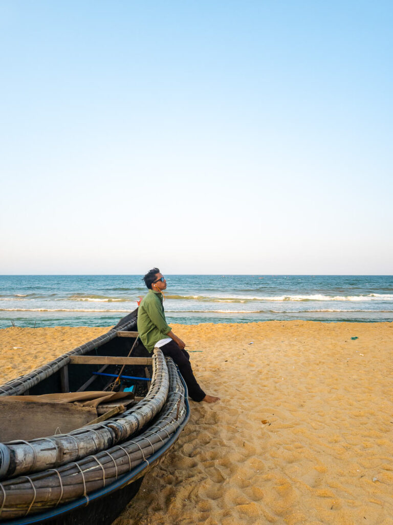 A traveler sitting on a wooden boat resting on the sand at a quiet beach near Hue.