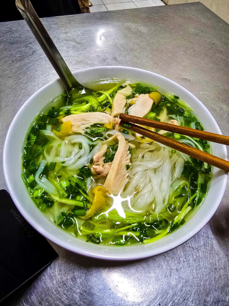 A steaming bowl of chicken pho with fresh herbs and lime at a local street food stall.