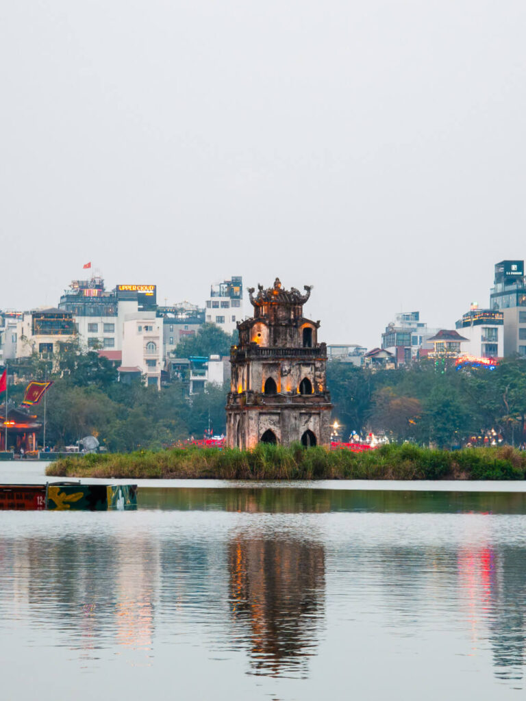 The historic Turtle Tower standing alone on a small island in the middle of the green waters of Hoan Kiem Lake during the day.