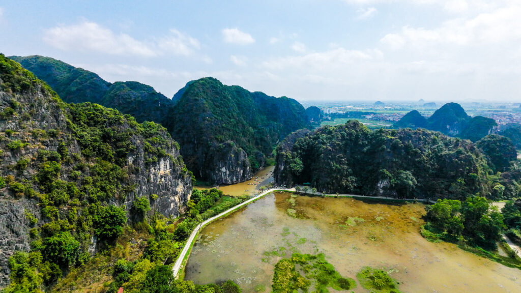 A wide drone shot showing the massive limestone karsts surrounding Thai Vi Temple.