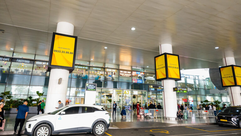 A busy exit gate at Noi Bai International Airport with travelers and taxis, illustrating how to get from Hanoi airport to Old Quarter.
