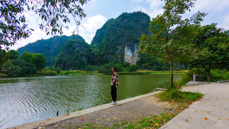 A solo traveler standing near a quiet, scenic lake while figuring out how to spend one day in Tam Coc away from the crowds.