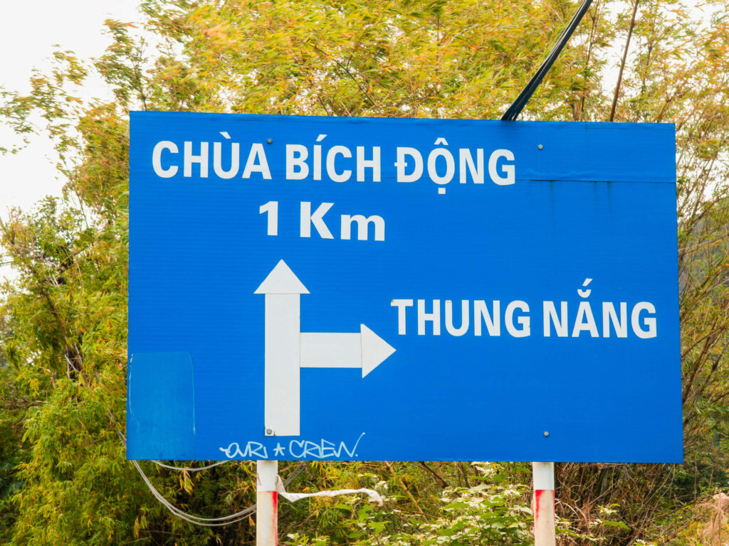 A rustic wooden signpost pointing towards local homestays and hidden attractions along a quiet dirt road.