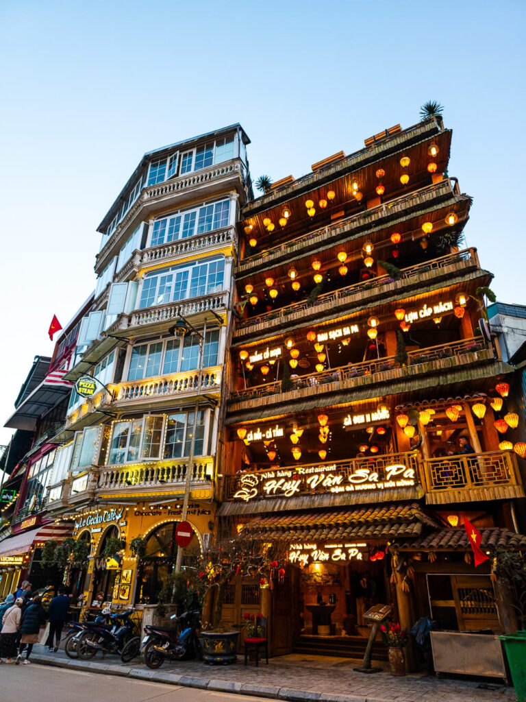 A close-up evening shot of a French-style building in Sapa illuminated with warm string lights as dusk sets in.