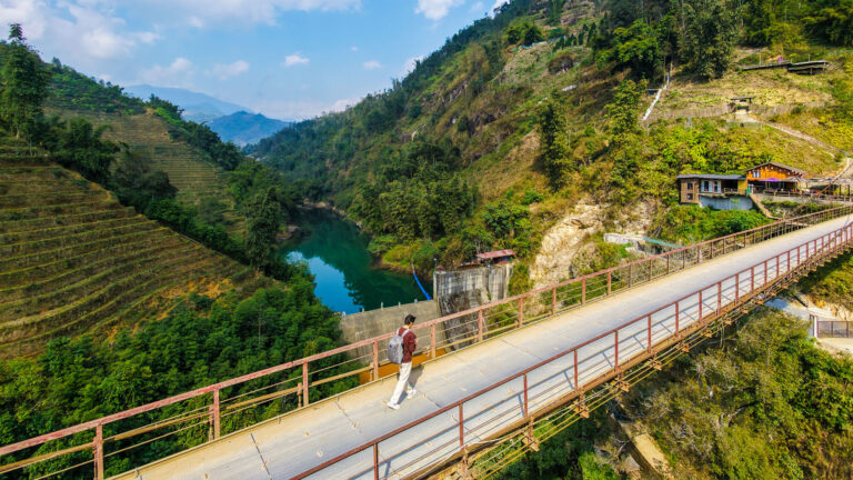 A traveler with an orange backpack walking across a suspension bridge during a Sapa trekking without a guide experience in Vietnam.