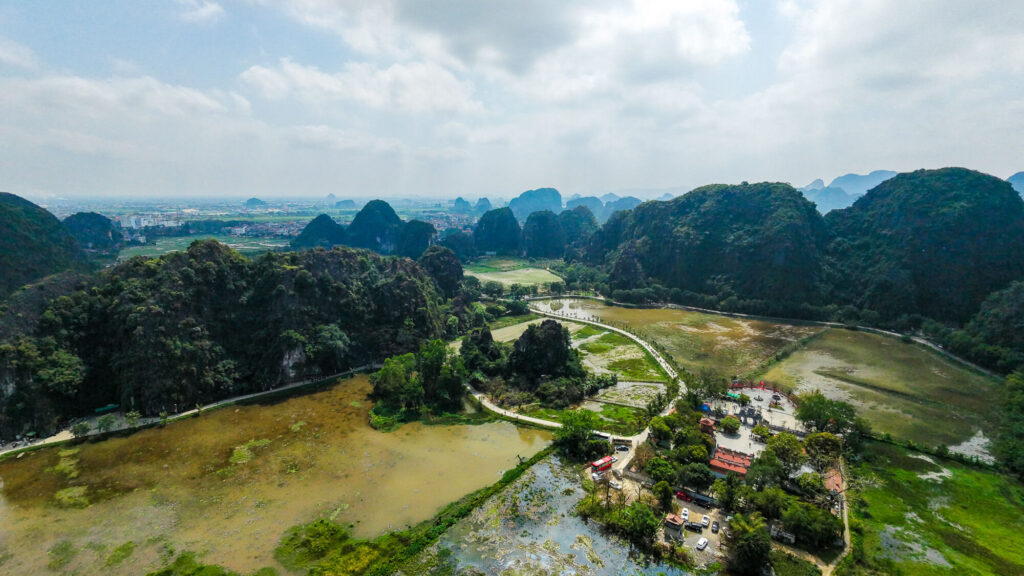 Aerial drone view looking down at the ancient Thai Vi Temple nestled perfectly at the base of massive limestone cliffs.
