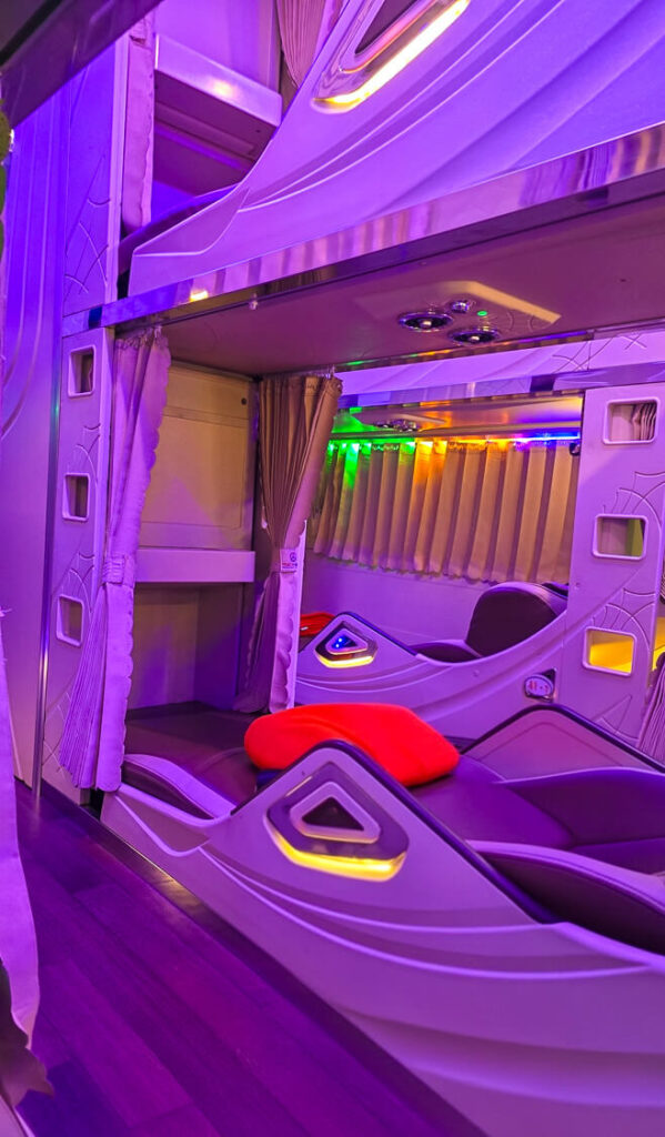 Wide shot of a modern Vietnamese sleeper bus interior showing two tiers of horizontal sleeping berths and an illuminated central aisle.