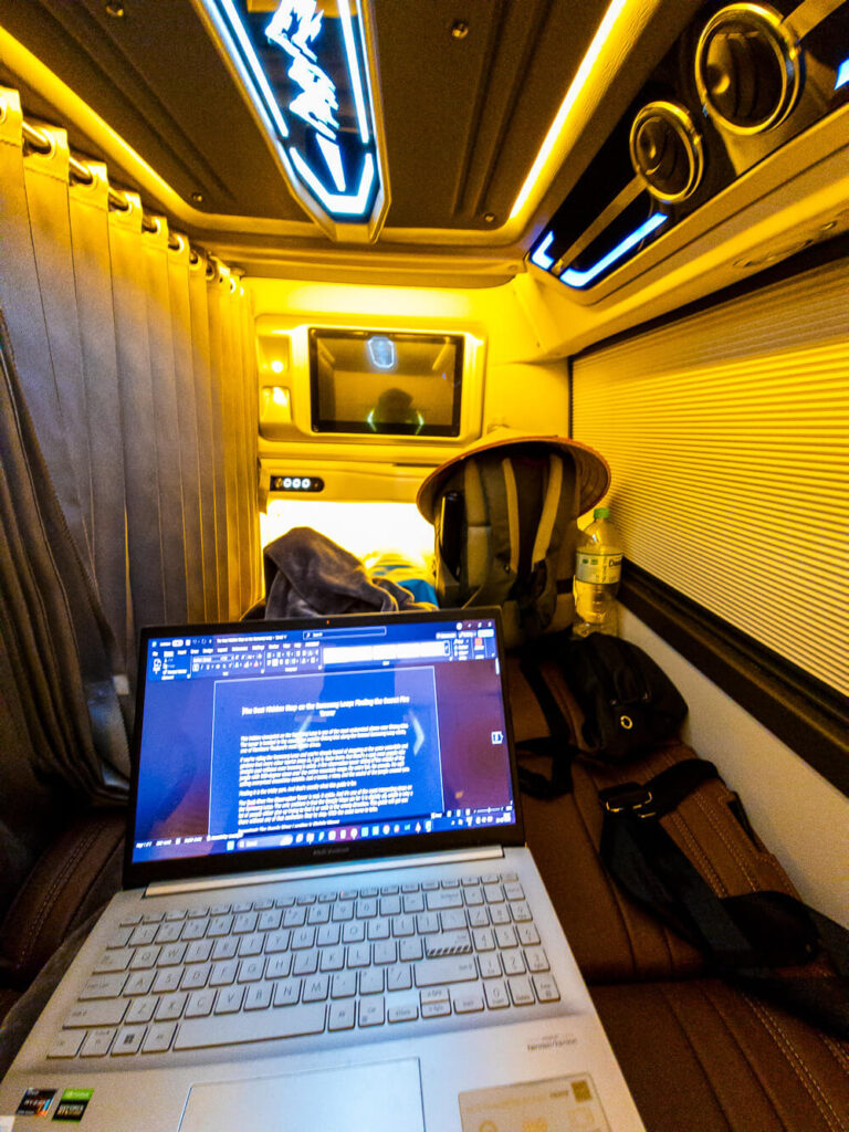 Travel writer working on a laptop inside a private HK busline sleeper cabin while traveling overnight.