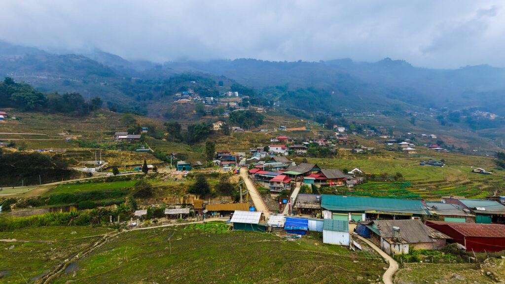 Aerial drone view of Lao Chai village showing traditional wooden houses nestled among vast green rice terraces in Sapa.