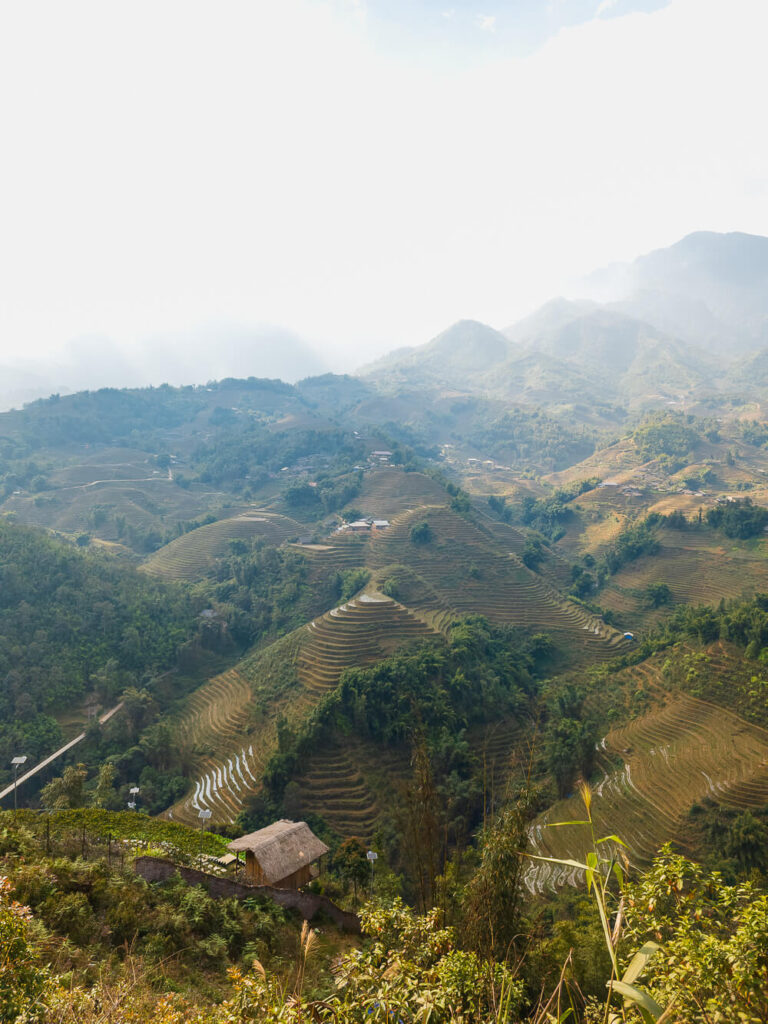 A wide-angle landscape shot of layered rice paddies and distant mist-covered mountains in Northern Vietnam.