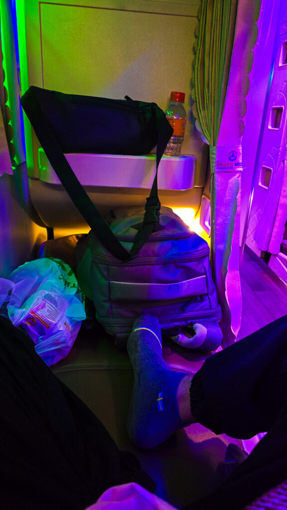 Travel blogger sitting inside a standard flat-reclining lower berth of a Vietnamese overnight sleeper bus.