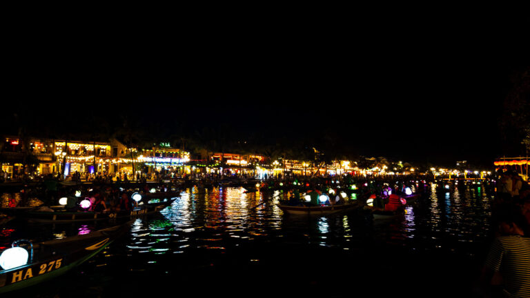 Traditional wooden boats with glowing lanterns on the Thu Bon River at night, a beautiful sight after traveling from Da Nang Airport to Hoi An.