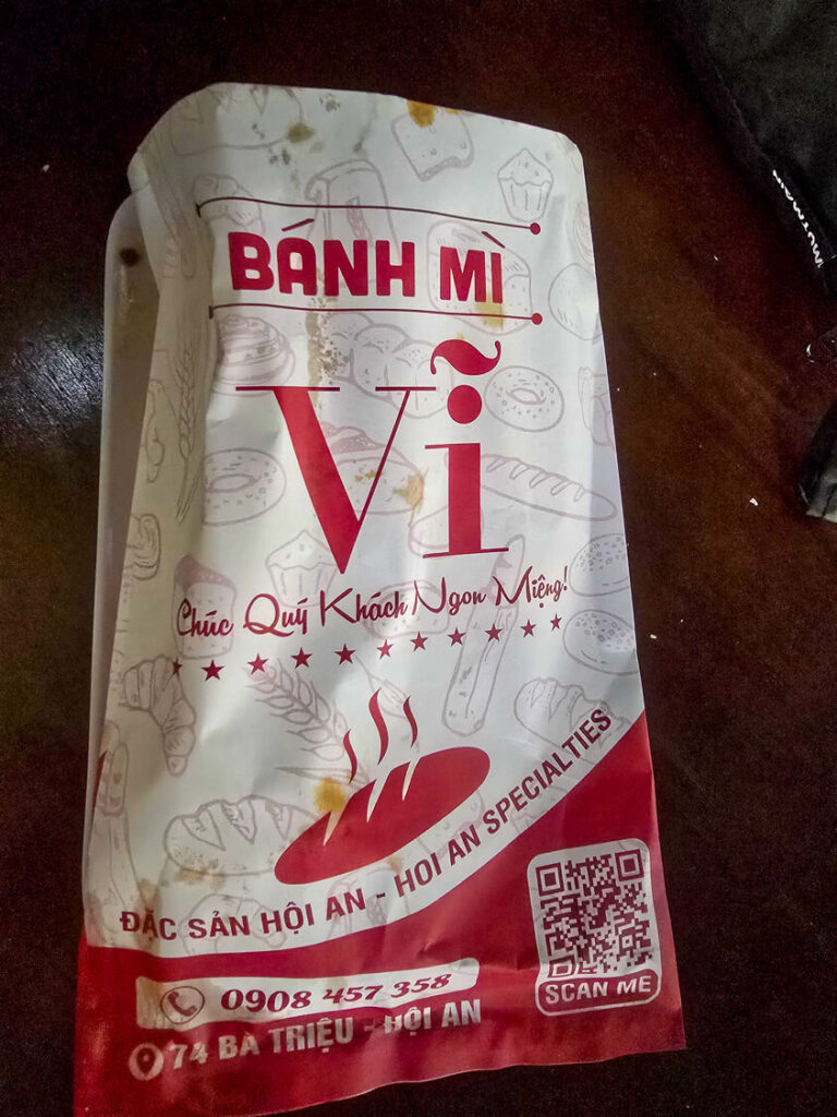 The brightly colored glass cover and street signage of a local Banh Mi food cart in Vietnam.