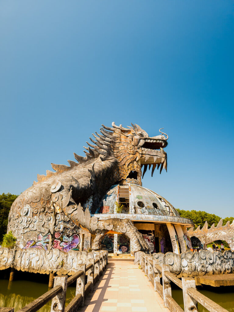 A massive, decaying three-story dragon structure rising from an empty lake at the Ho Thuy Tien abandoned water park in Hue.