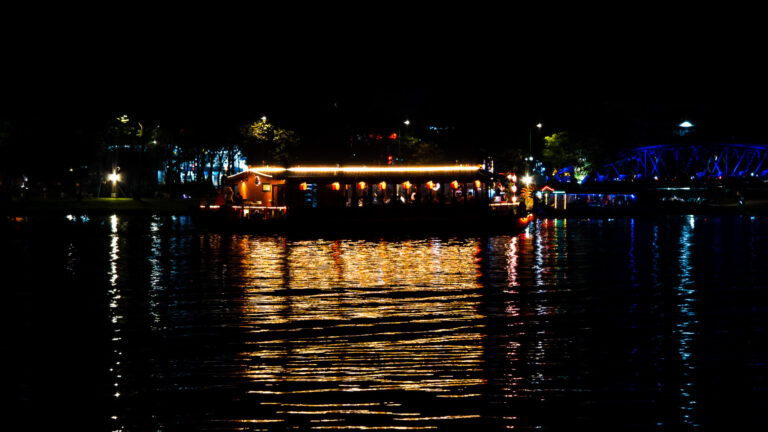 A brightly lit boat restaurant floating on the dark water of the Perfume River at night.