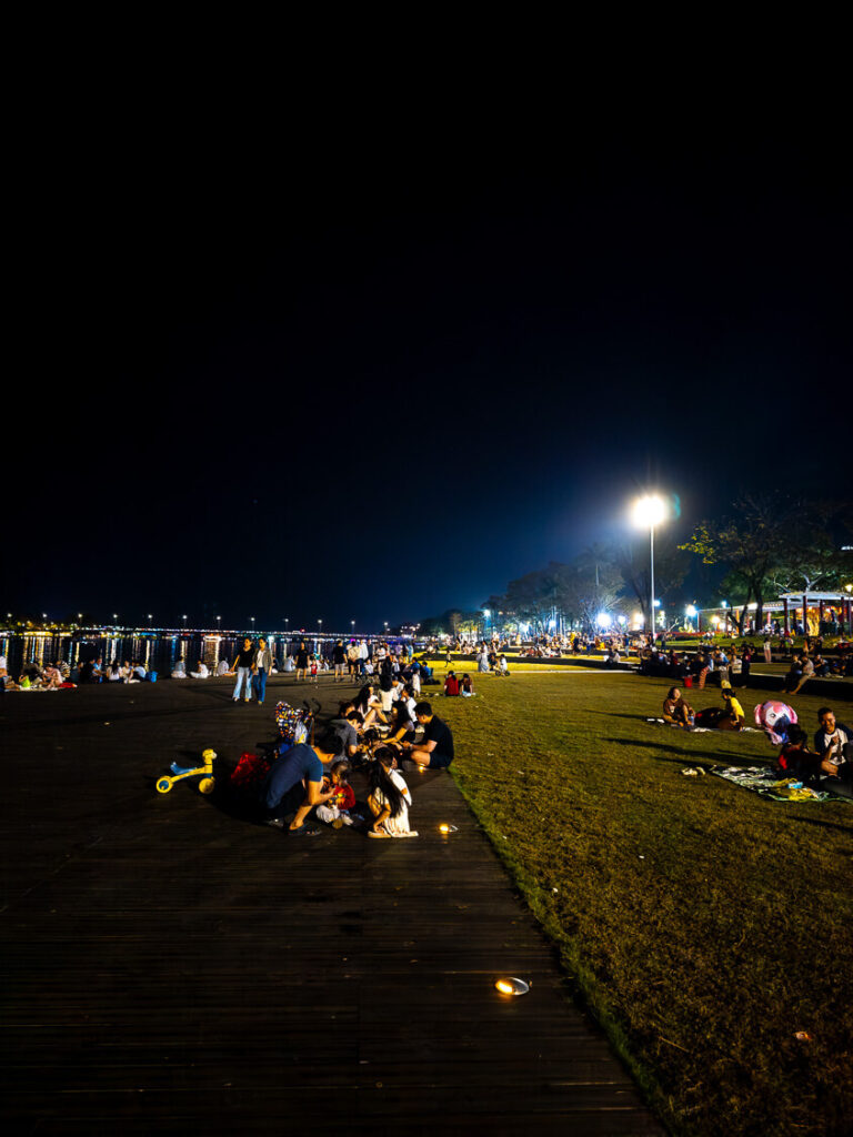 Local Hue residents and families sitting on their scooters and the banks of the Perfume River at night, enjoying street food under the city lights.