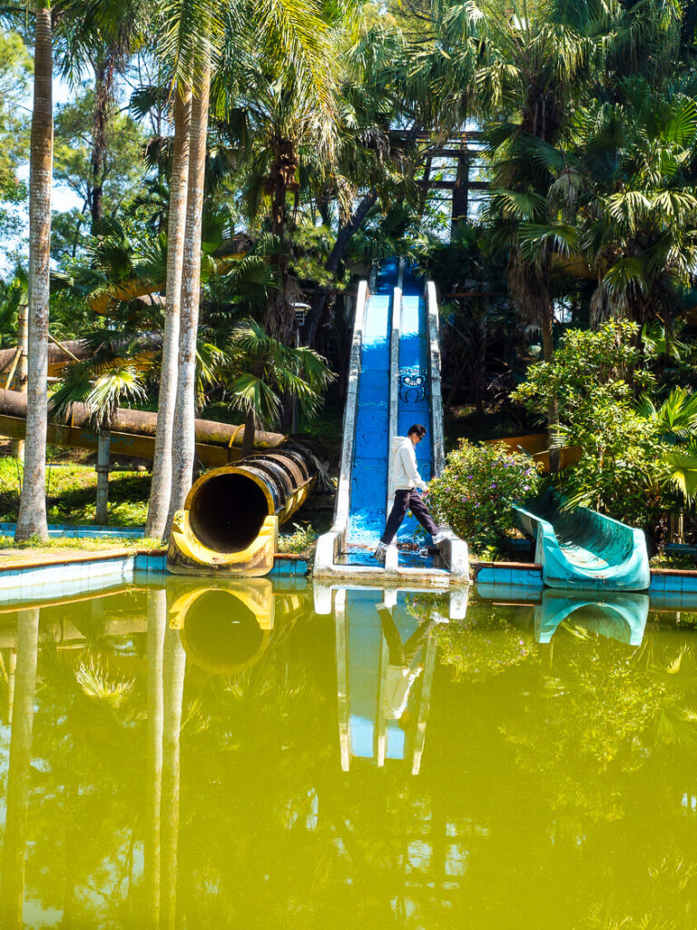 Traveler walking down the dry decaying waterslides reclaimed by nature at the abandoned theme park