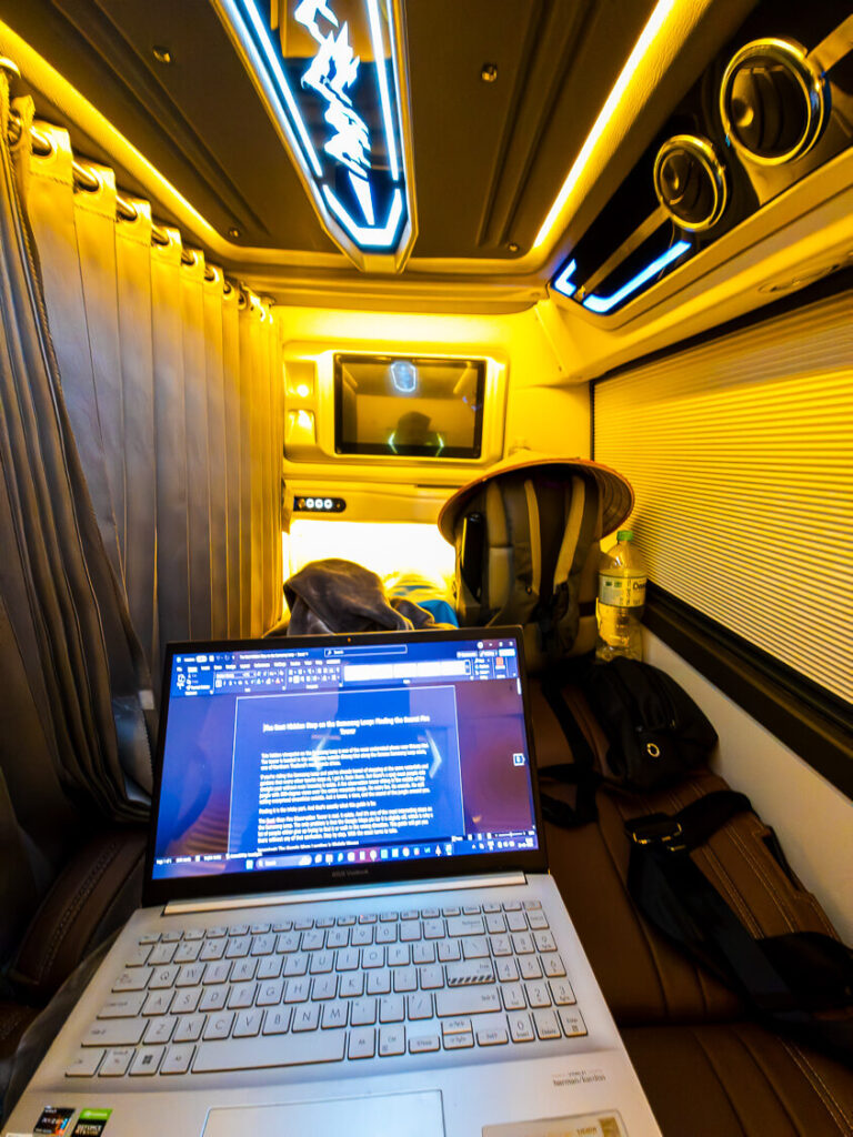 A solo traveler sitting comfortably inside the private cabin of an overnight sleeper bus in Vietnam working on a laptop.