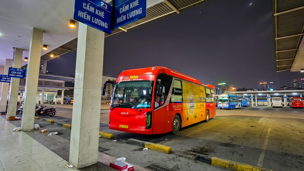 A bright red sleeper bus parked at a transport terminal at night, illustrating essential Vietnam sleeper bus tips for overnight travelers.