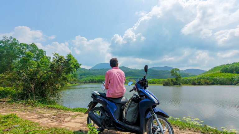 A backpacker sitting on a rented scooter overlooking a lush green valley, representing the freedom of a low Vietnam travel budget.