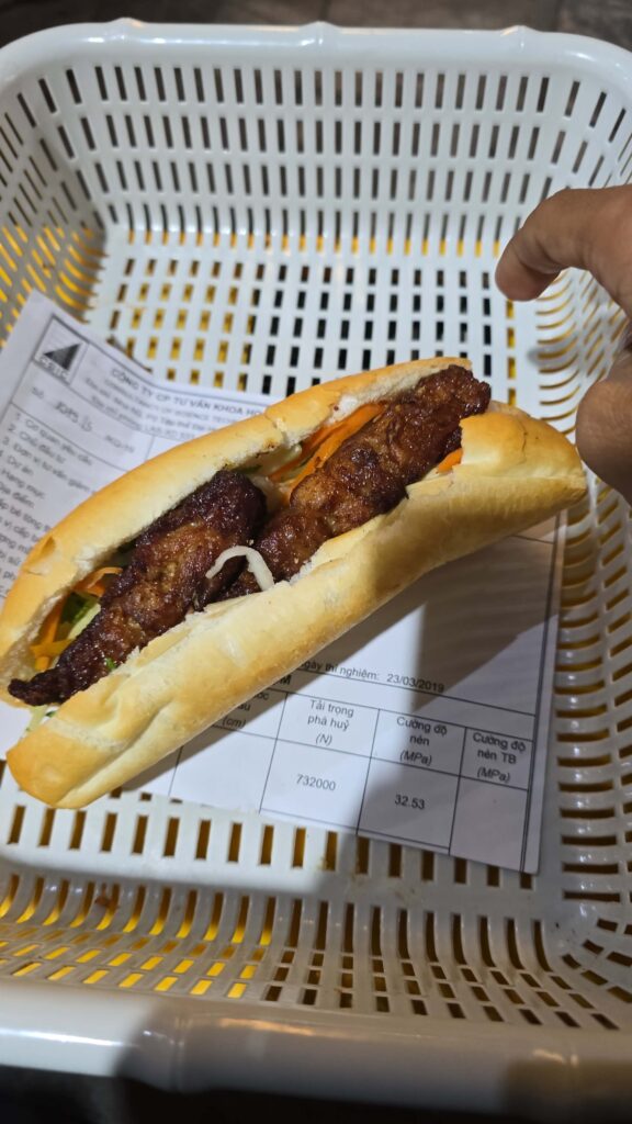 Close up of a crispy Vietnamese Banh Mi sandwich loaded with meat and fresh herbs from a local street vendor.