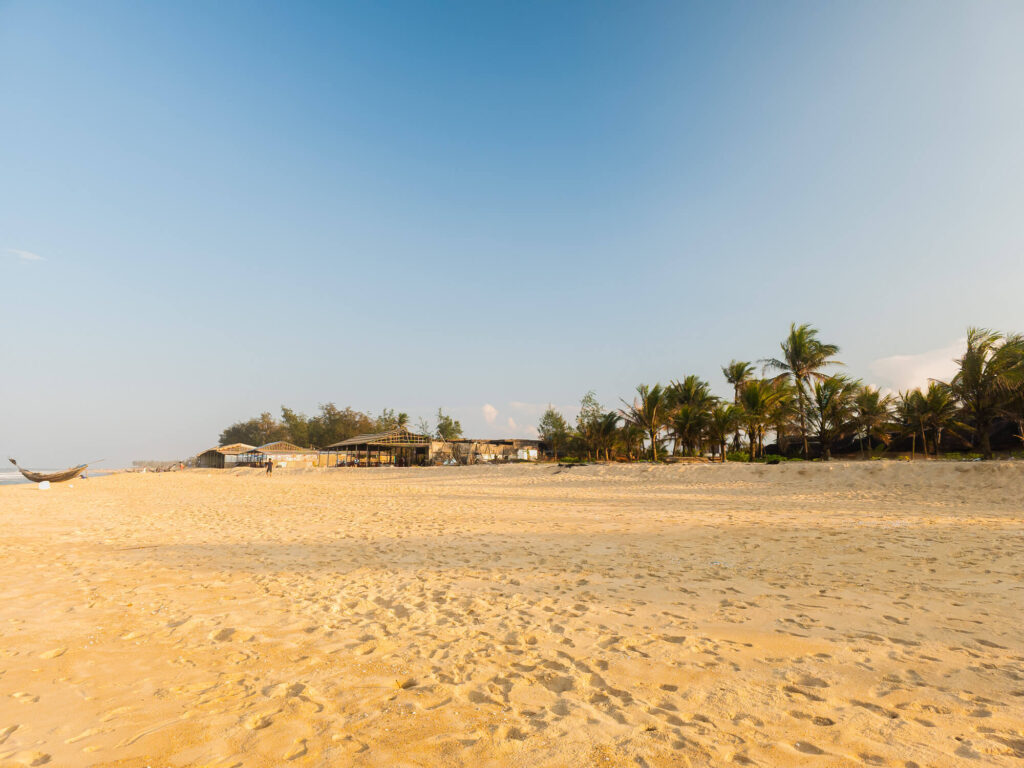 A wide landscape shot showing the empty sands and calm, flat waters of Thuan An Beach near Hue on a quiet weekday morning.